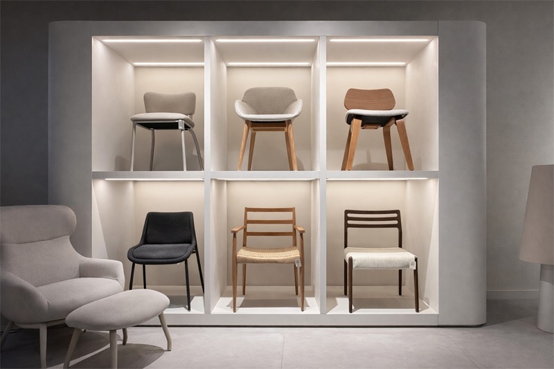 Exposici&oacute;n de sillas de dise&ntilde;o en estanter&iacute;a iluminada, con modelos tapizados y de madera en diferentes estilos y acabados.