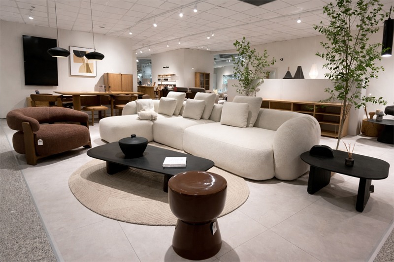 Sal&oacute;n contempor&aacute;neo con sof&aacute; curvo en color blanco, mesa de centro negra, mesa auxiliar y sill&oacute;n tapizado en tono marr&oacute;n.